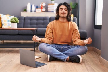Genç latin adam yoga yapıyor. Evde yerde oturuyor.