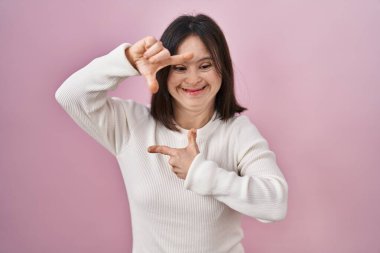 Pembe arka planda durup gülümseyen, elleri ve parmakları gülen yüzlü bir kadın. yaratıcılık ve fotoğrafçılık kavramı. 