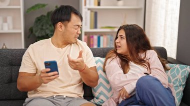 Kadın ve erkek akıllı telefon kullanıyor. Kanepede oturmuş tartışıyorlar.