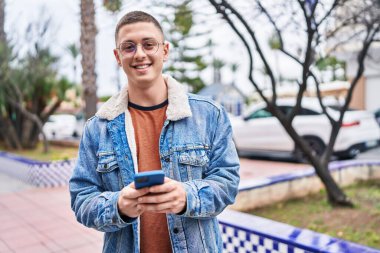 Parkta akıllı telefon kullanarak gülümseyen İspanyol genç adam.