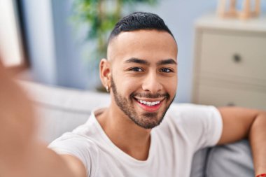Afrikalı Amerikalı adam evdeki kanepede otururken kamerayla selfie çekiyor.