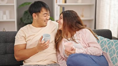 Man and woman couple sitting on sofa drinking coffee at home