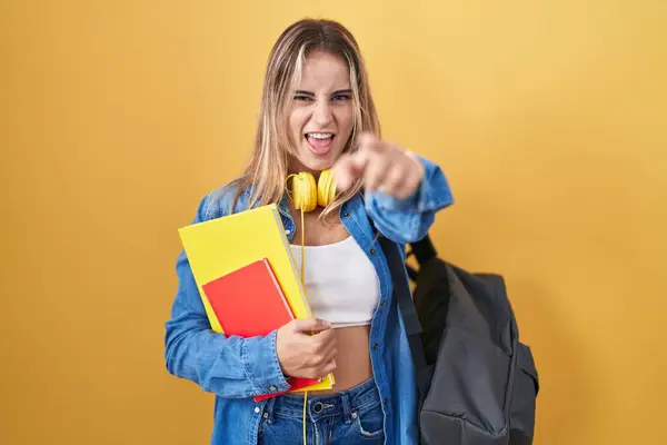若い金髪の女性は学生のバックパックを身に着け カメラに不満と欲求不満を指摘する本を持って 怒りと怒り — ストック写真