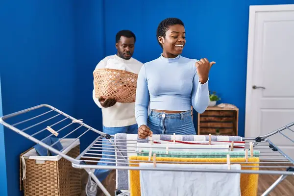 Young African American Couple Hanging Clothes Clothesline Pointing Thumb Side — Stock Photo, Image
