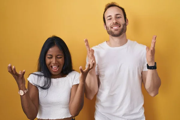 stock image Interracial couple standing over yellow background celebrating mad and crazy for success with arms raised and closed eyes screaming excited. winner concept 