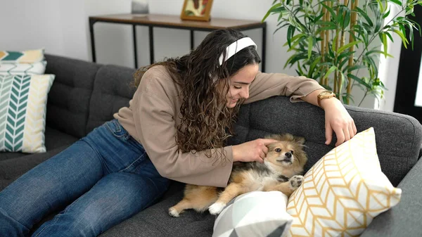 Young hispanic woman with dog listening to music sitting on sofa at home
