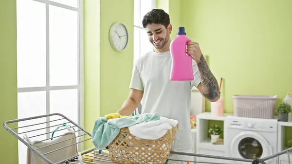 年轻人手里拿着洗涤剂瓶子 站在洗衣房的晾衣绳旁 — 图库照片