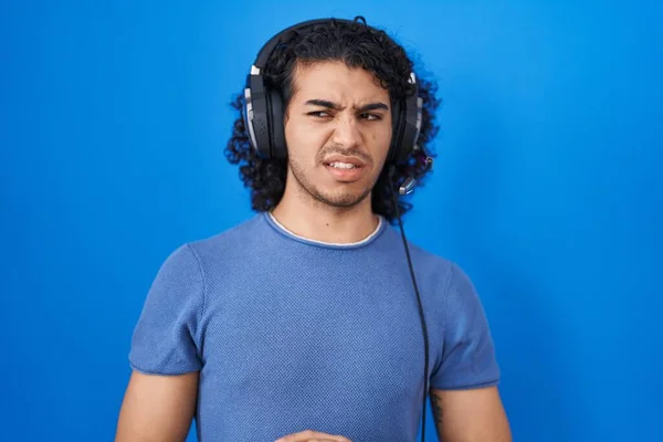 Ισπανόφωνος Άνθρωπος Σγουρά Μαλλιά Ακούγοντας Μουσική Χρησιμοποιώντας Ακουστικά Αηδιασμένος Έκφραση — Φωτογραφία Αρχείου