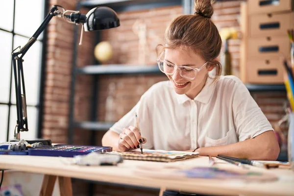在艺术工作室 年轻的金发女子带着自信的笑容在笔记本上画画 — 图库照片