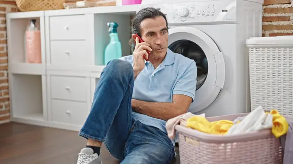 中年男子在洗衣房用智能手机在等洗衣机 — 图库照片