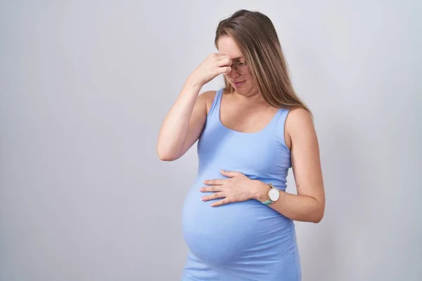 年轻的孕妇站在白色的背景上 疲倦地揉揉鼻子和眼睛 感到疲倦和头痛 压力和挫败感概念 — 图库照片