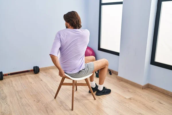 Middle age man sitting on chair stretching at sport center