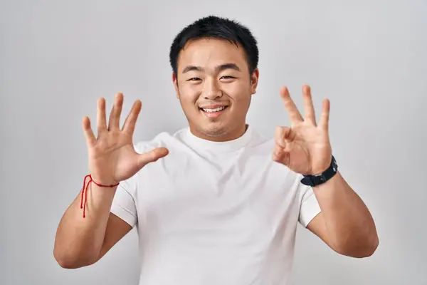 年轻的中国男人站在白种人的背景上 用八号手指指指指点点 自信而快乐地微笑着 — 图库照片