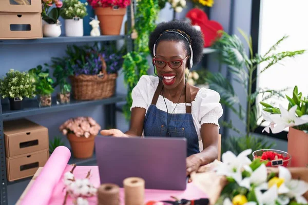 African woman with curly hair working at florist shop doing video call celebrating achievement with happy smile and winner expression with raised hand