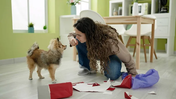 Young hispanic woman with dog angry for breaking paper bag at dinning room