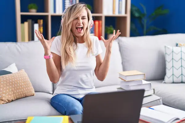 自宅でコンピュータのラップトップを使用して勉強している若い金髪の女性は 腕を上げて興奮する目を閉じた成功のために狂気とクレイジーを祝います 優勝コンセプト — ストック写真