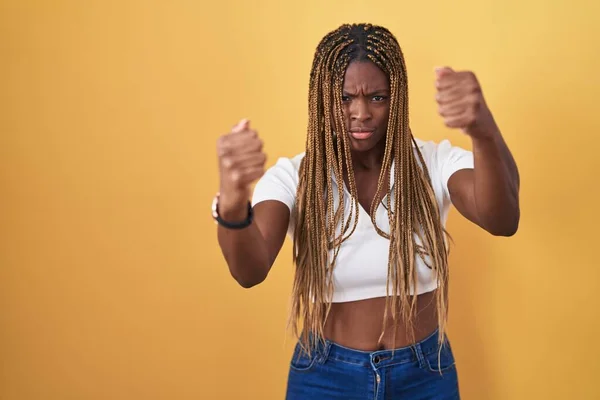 Африканская Американка Плетеными Волосами Стоящая Жёлтом Фоне Злая Безумная Поднимающая — стоковое фото