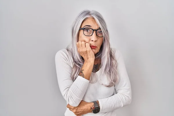 白い背景の上に立っている灰色の髪を持つ中年の女性は 口に噛まれた爪の手でストレスと神経質に見えます 不安問題 — ストック写真