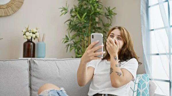 Jonge Vrouw Met Smartphone Zitten Bank Verrast Thuis — Stockfoto