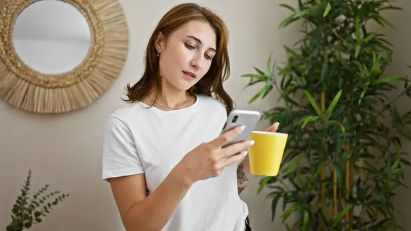 Genç Bir Kadın Elinde Kahve Fincanıyla Evde Akıllı Telefon Kullanıyor — Stok fotoğraf