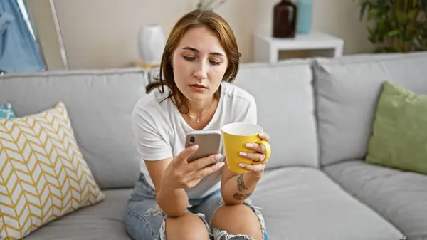 自宅でスマートフォンを飲むコーヒーを使用して若い女性 — ストック写真