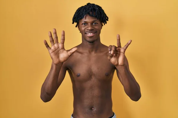 ドレッドロックを持つ若いアフリカ人男性は シャツレスで立って 自信と幸せを笑いながら指のナンバー7を指で指さす — ストック写真