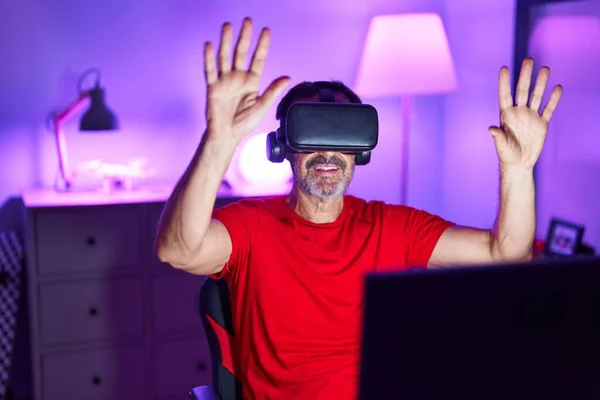 Middle age man streamer playing video game using virtual reality glasses at gaming room