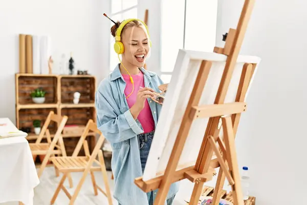 Young caucasian woman artist listening to music drawing at art studio