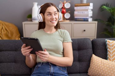 Young beautiful woman watching video on touchpad sitting on sofa at home