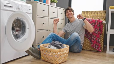 Çamaşırhanede yerde oturmuş dans eden Latin asıllı genç bir adam.