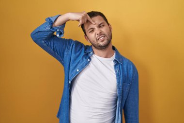 Sarı arka planda dikilen İspanyol adam alnındaki sivilceden mutsuz olduğunu gösteriyor, siyah noktalı çirkin bir enfeksiyon. sivilce ve deri problemi 