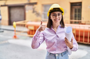 İnşaat alanında mimar şapkası takan İspanyol kız mutlu ve olumlu gülümsüyor, başparmağıyla mükemmel ve onay işareti yapıyor. 