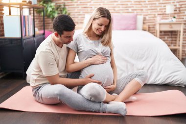 Kadın ve erkek, yatak odasındaki yoga minderinde göbeğine dokunuyor.