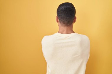 Sarı arka planda duran yakışıklı İspanyol adam çapraz kollarla başka tarafa bakıyor. 