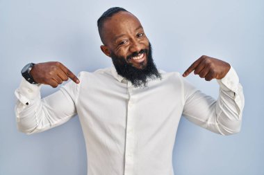Mavi arka planda duran Afro-Amerikan bir adam. Yüzünde bir gülümsemeyle, kendini gururlu ve mutlu olarak gösteriyor.. 