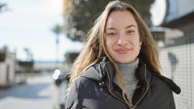 Sokakta kendine güvenen beyaz kadın gülümsüyor.