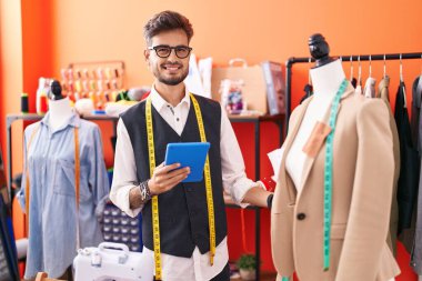 Genç İspanyol terzi dokunmatik ped kullanıyor. Atölyede duruyor.