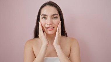 Genç, güzel, İspanyol bir kadın, kendine güvenen, pembe arka planda masaj yapan, gülümseyen.