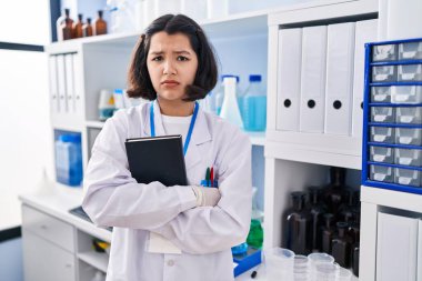 Young hispanic woman working at scientist laboratory skeptic and nervous, frowning upset because of problem. negative person. 