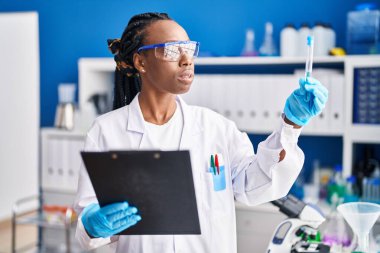 African american woman scientist holding test tube reading document at laboratory