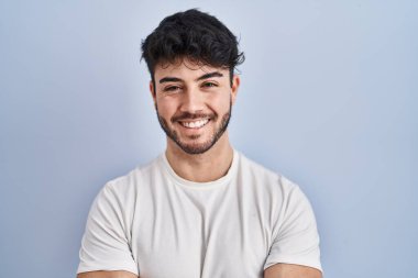 Beyaz arka planda sakallı İspanyol bir adam kollarını kavuşturup kameraya bakarken gülümsüyor. pozitif kişi. 