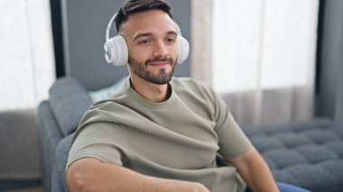 Genç İspanyol adam evdeki kanepede oturmuş müzik dinliyor.