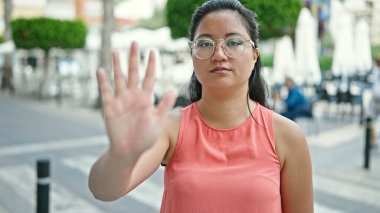 Genç Çinli bir kadın sokakta el hareketlerini durduruyor.