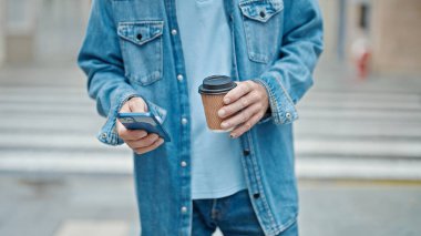 Orta yaşlı bir adam akıllı telefon kullanıyor ve sokakta kahve içiyor.