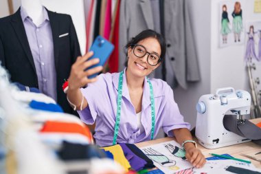 Dikiş makinesi kullanan güzel İspanyol kadın terzide akıllı telefondan selfie çekiyor.
