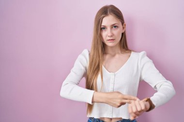 Pembe arka planda dikilen genç beyaz kadın zamanı, sabırsızlığı ve gecikmeyi izlemek için acele ediyor. 