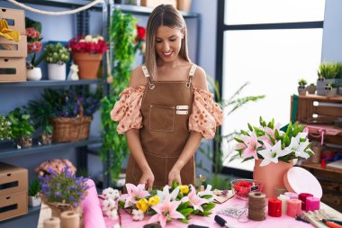 Young beautiful hispanic woman florist make bouquet of flowers at flower shop