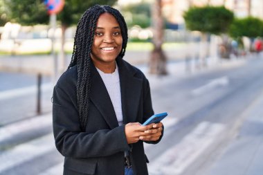 Afro-Amerikalı kadın sokakta akıllı telefon kullanarak kendine güveniyor.