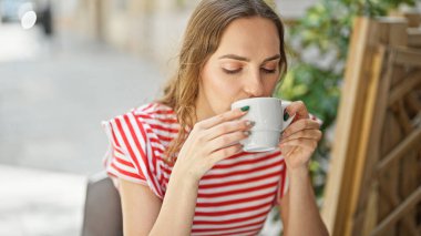 Kahve dükkanının terasında bir fincan kahve içen genç sarışın kadın.