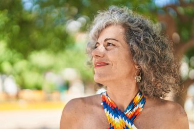 Middle age grey-haired woman smiling confident looking to the sky at park